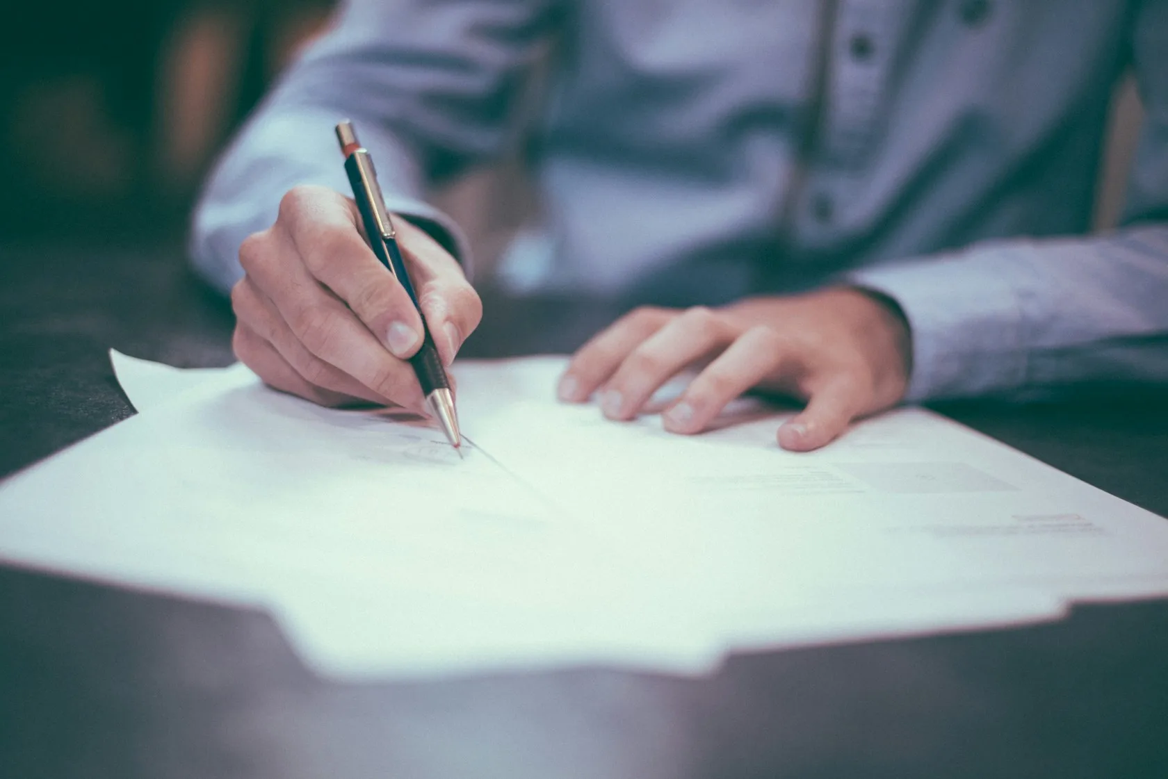 Persona firmando un contrato de préstamo sobre una mesa: autónomo y condición de consumidor
