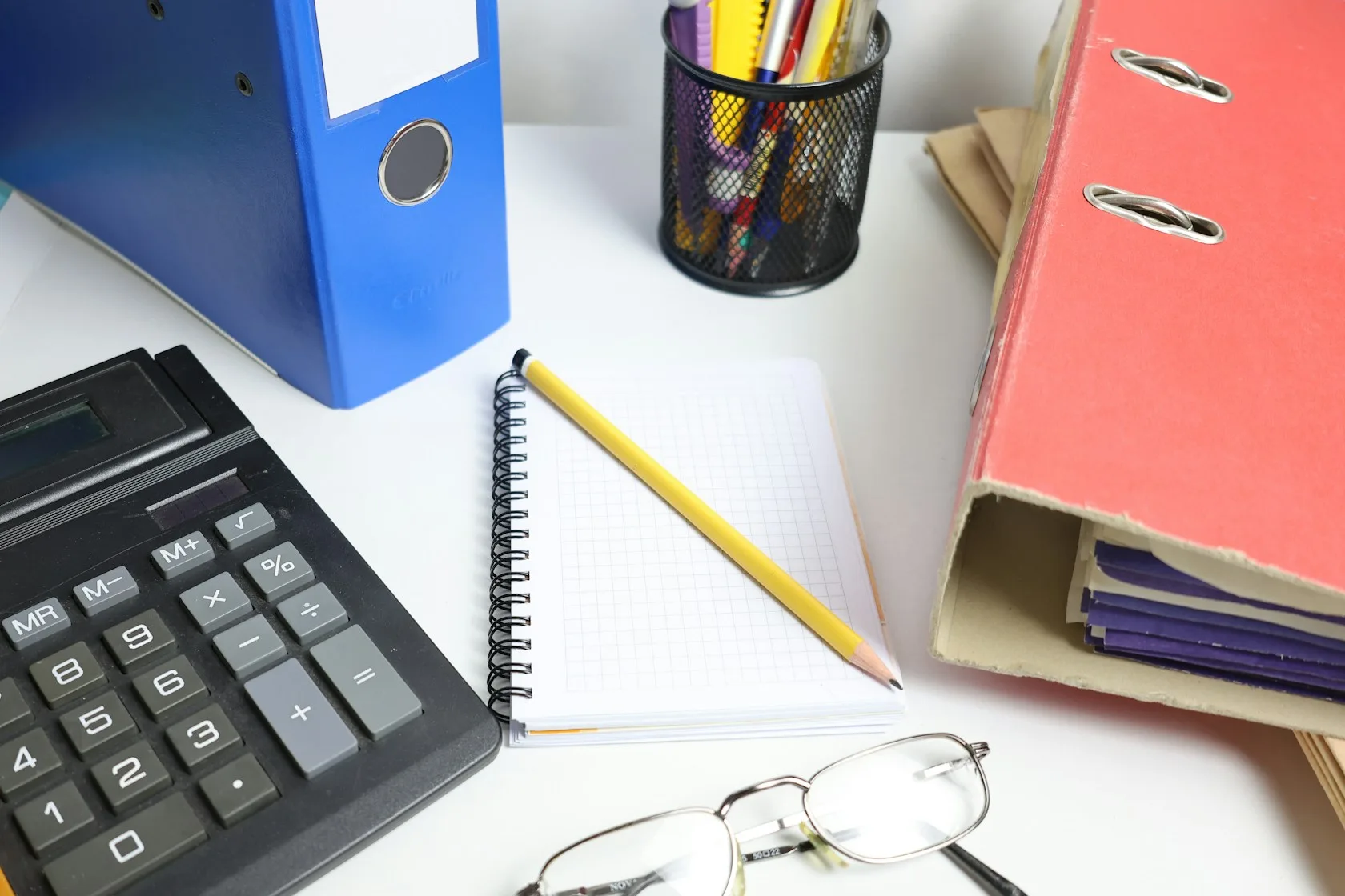 Escritorio con calculadora, carpetas, cuaderno y gafas para preparar la documentación de la Ley de Segunda Oportunidad