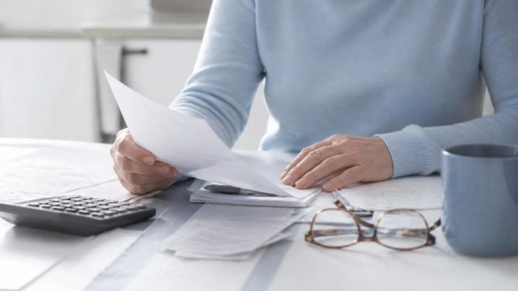 Manos revisando facturas y documentos familiares junto a una calculadora y gafas de lectura: endeudarse por ayudar a la familia