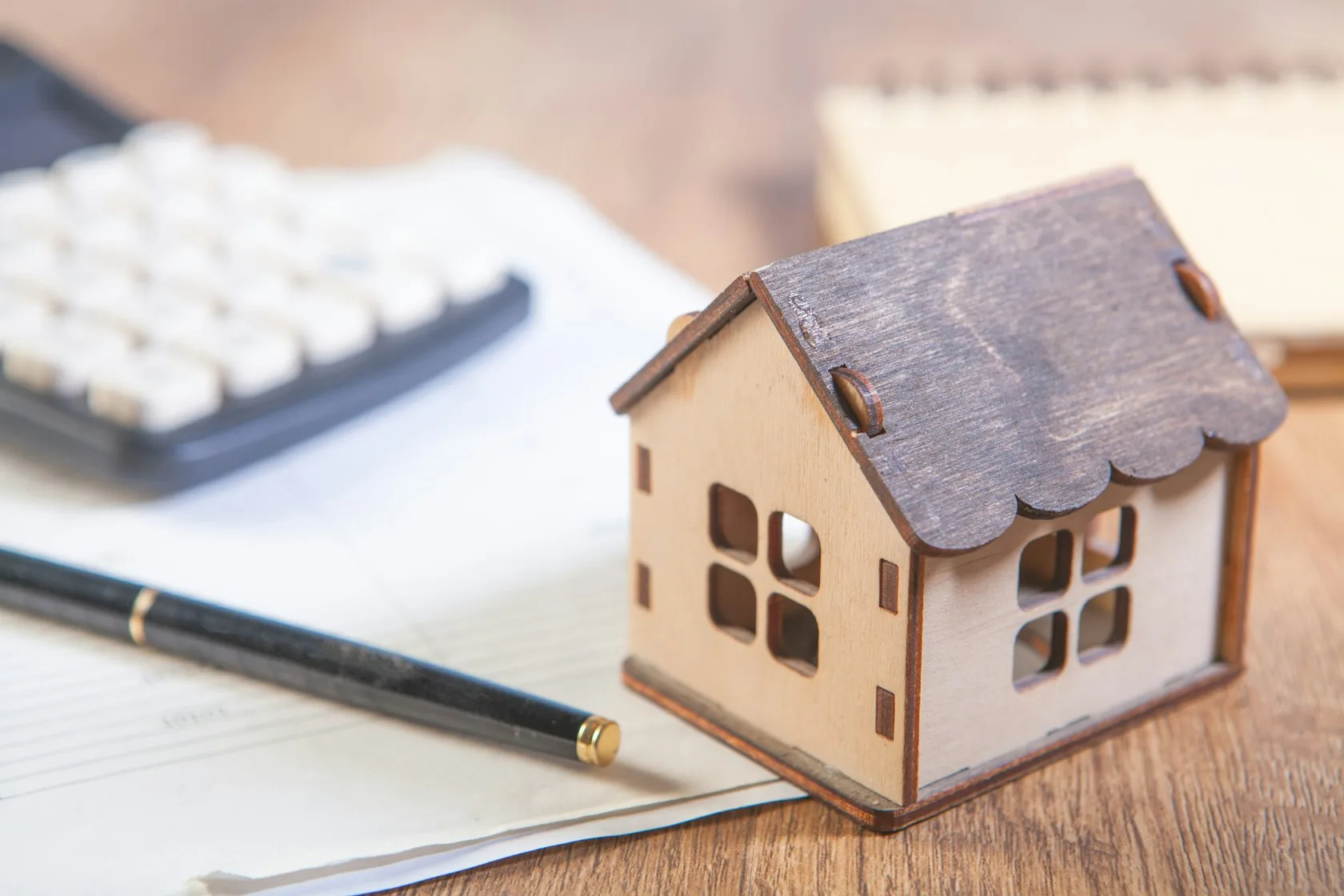 Casa de madera en miniatura junto a una calculadora y un bolígrafo para calcular la cuota de la hipoteca variable con la subida del euríbor