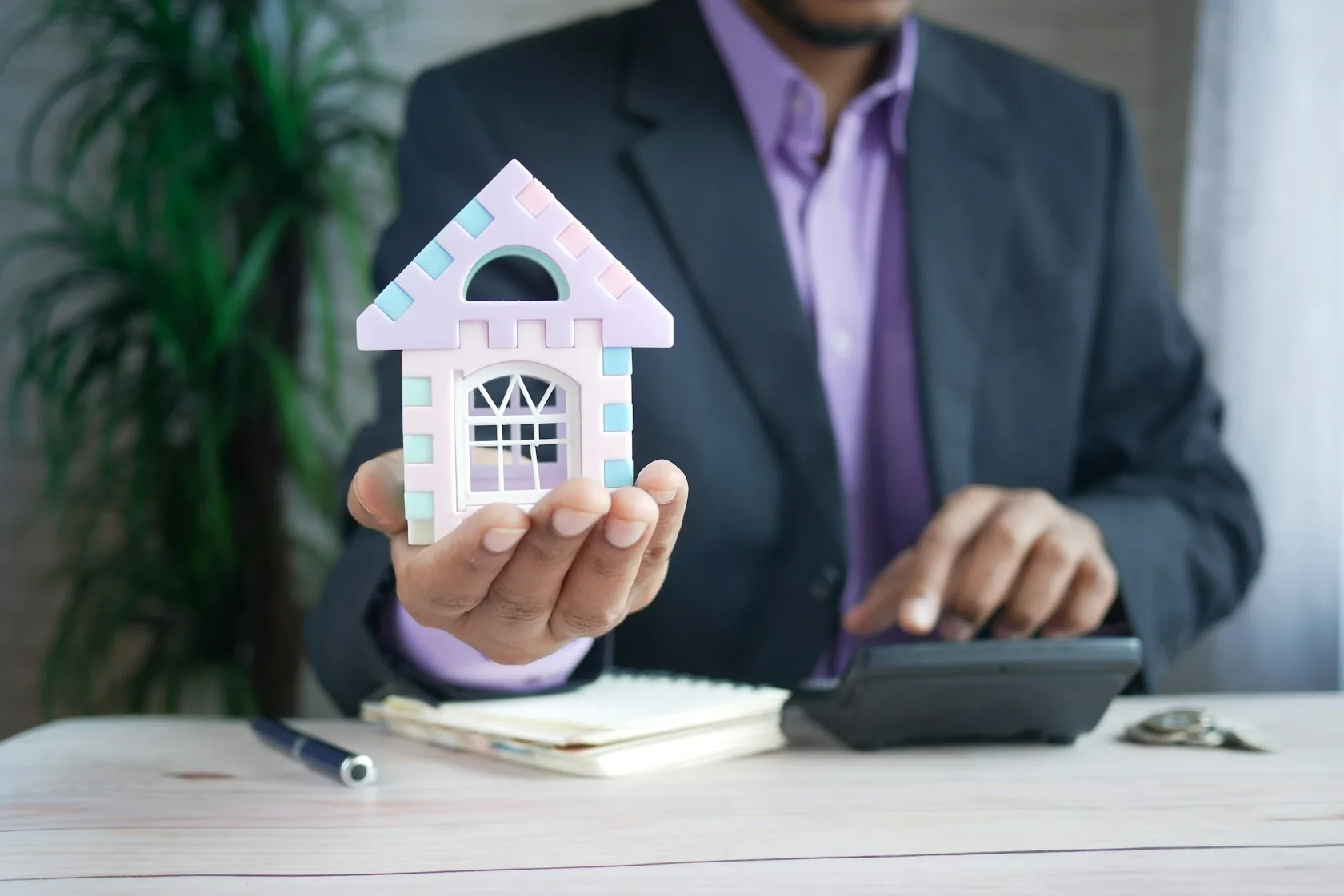 Hombre sosteniendo una casa en miniatura junto a una calculadora: hipoteca variable que no puedes pagar
